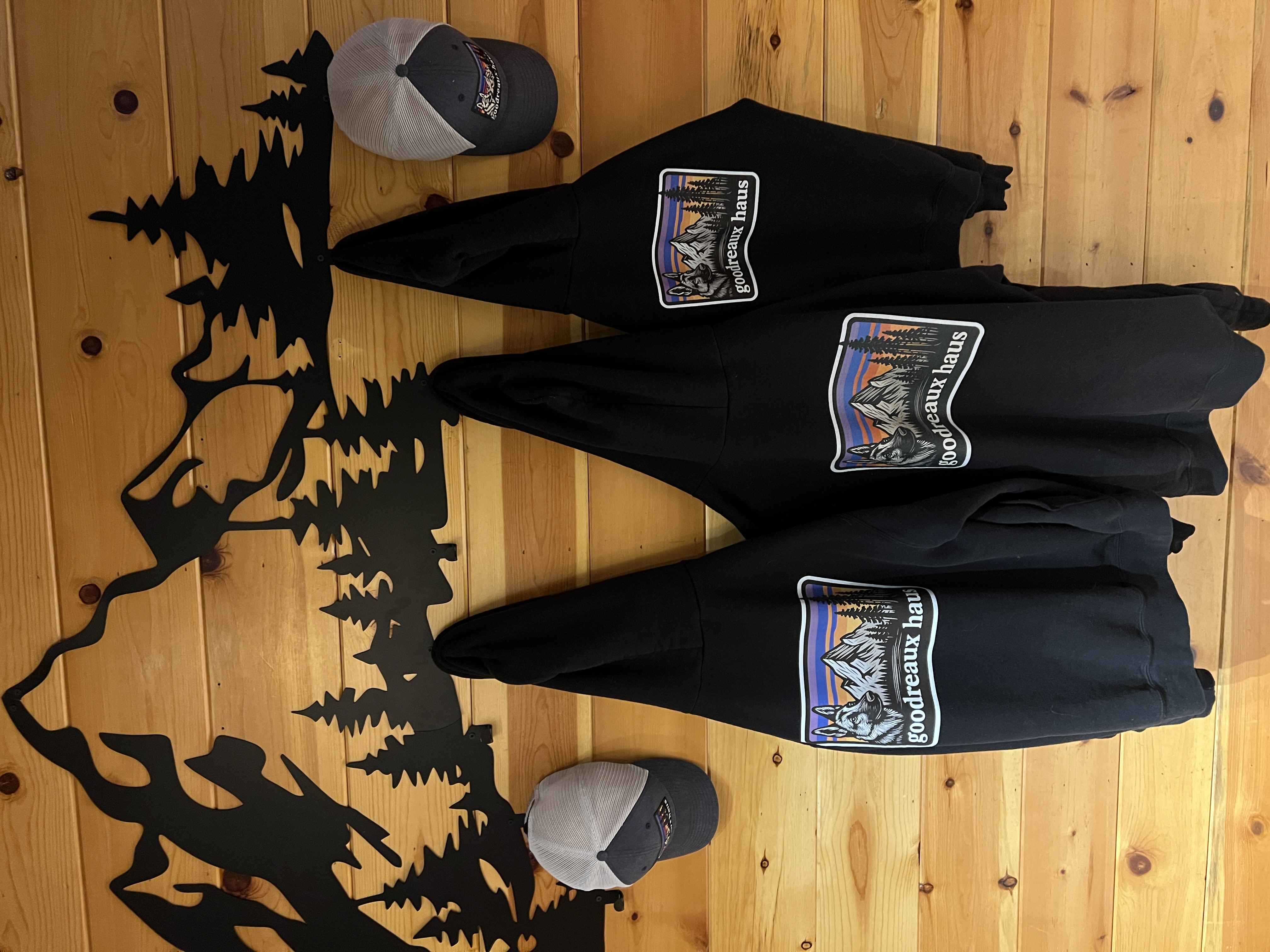 Goodreaux Haus hoodies and trucker hats hanging on a mountain wall rack